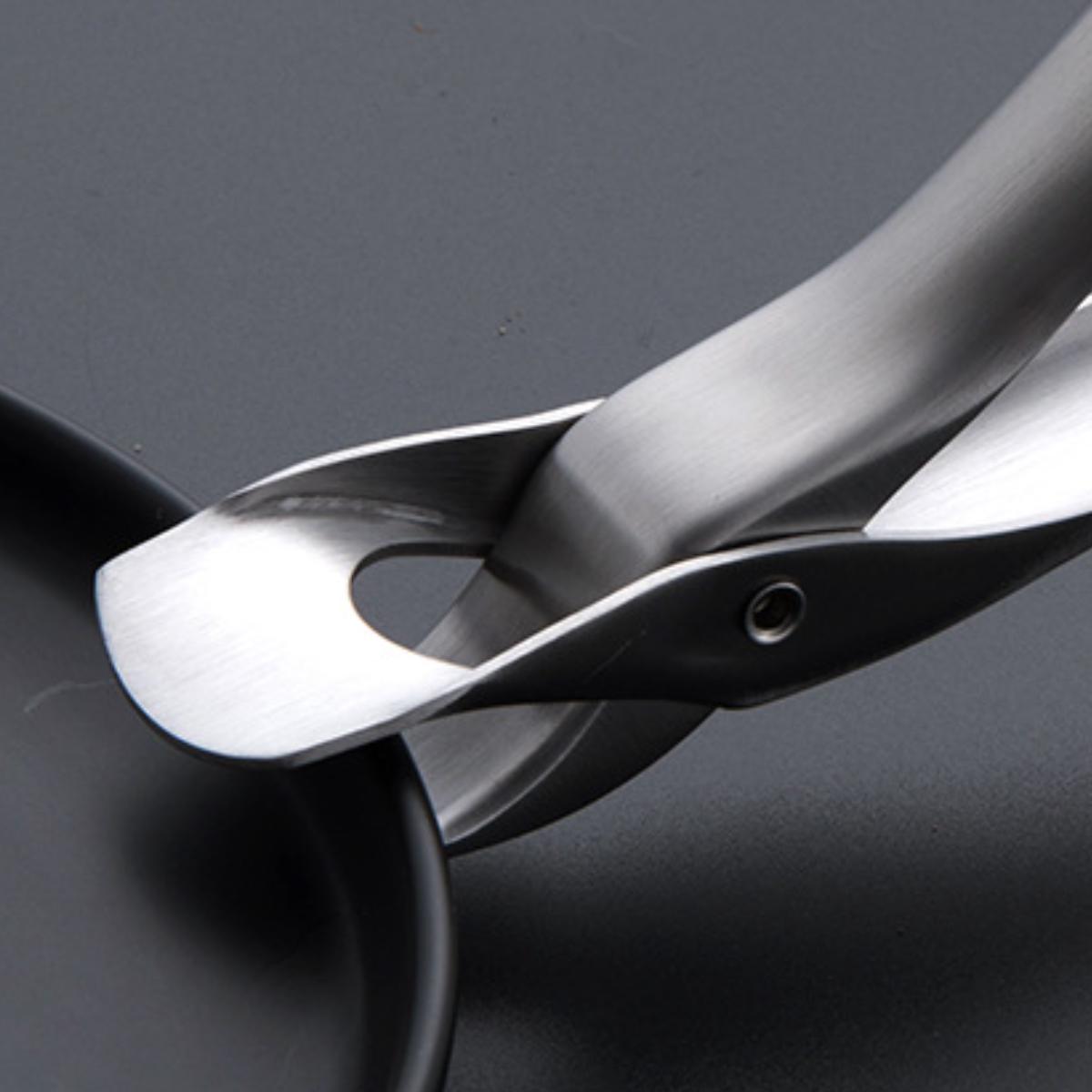 Nahaufnahme einer Edelstahlzange, die ein schwarzes Objekt hält. Die Zange hat ein einzigartiges Design.