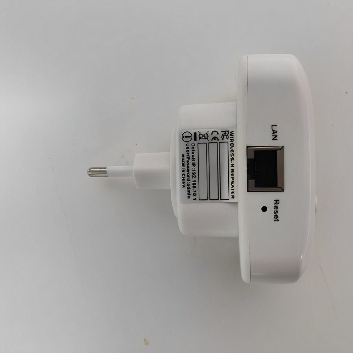 Weißer Wireless-N-Repeater mit Stecker, LAN-Anschluss und Reset-Taste auf weißer Oberfläche.