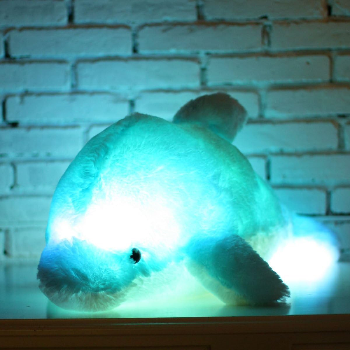 Ein leuchtendes Plüsch-Delphin-Spielzeug mit blauem Licht vor einem Backsteinmauer-Hintergrund.