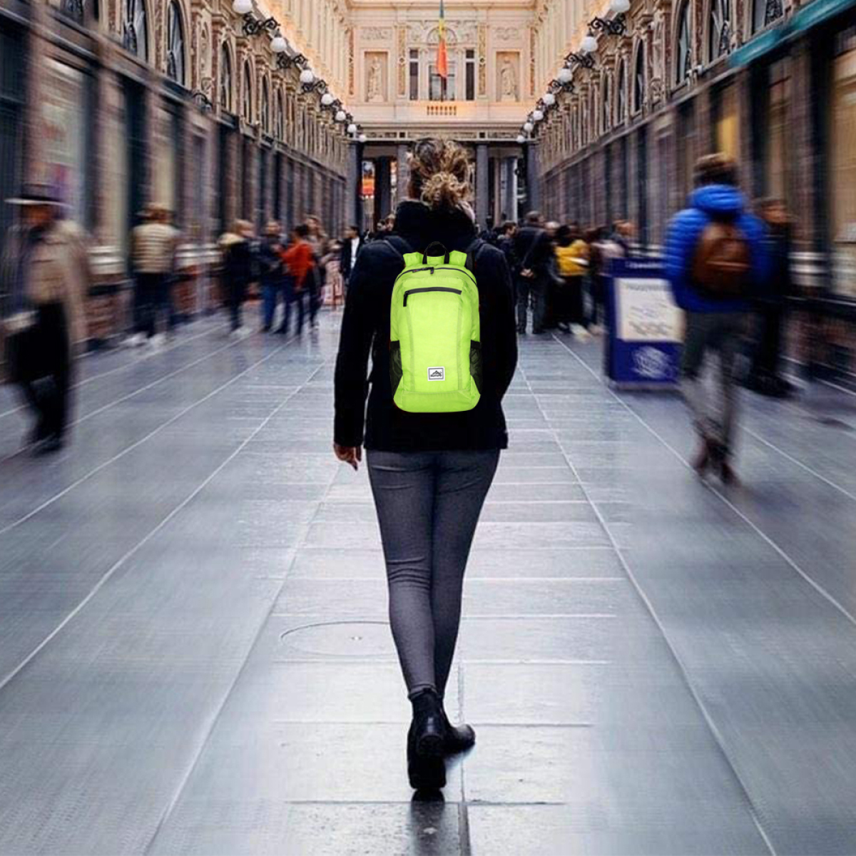 Frau mit neongrünem Rucksack geht in einem Flur.