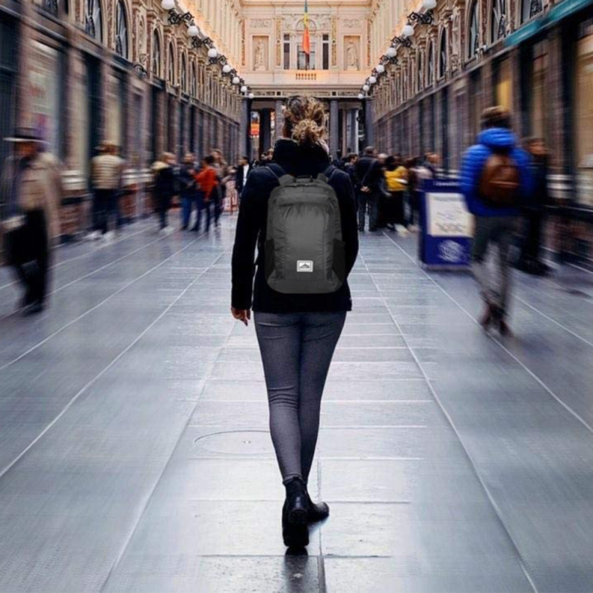 Frau geht in einem Flur mit einem Rucksack. Verschwommener Hintergrund mit Menschen.