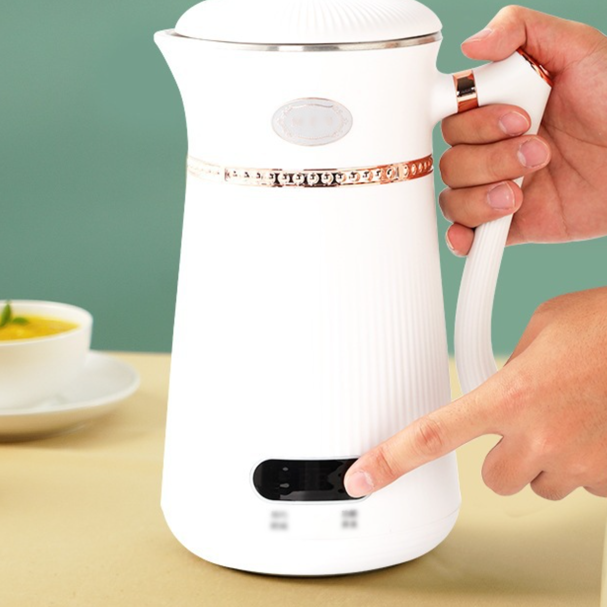 Weißer Wasserkocher, Hand drückt den Einschaltknopf. Eine Schüssel Suppe ist in der Nähe.