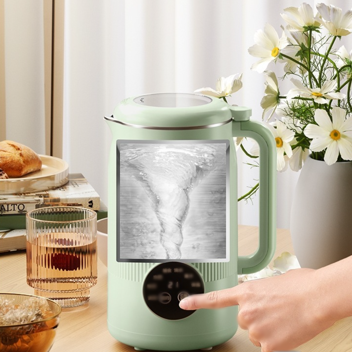 Grüner Wasserkocher mit Digitalanzeige. Eine Hand berührt die Taste. Weiße Blumen und Brot im Hintergrund.