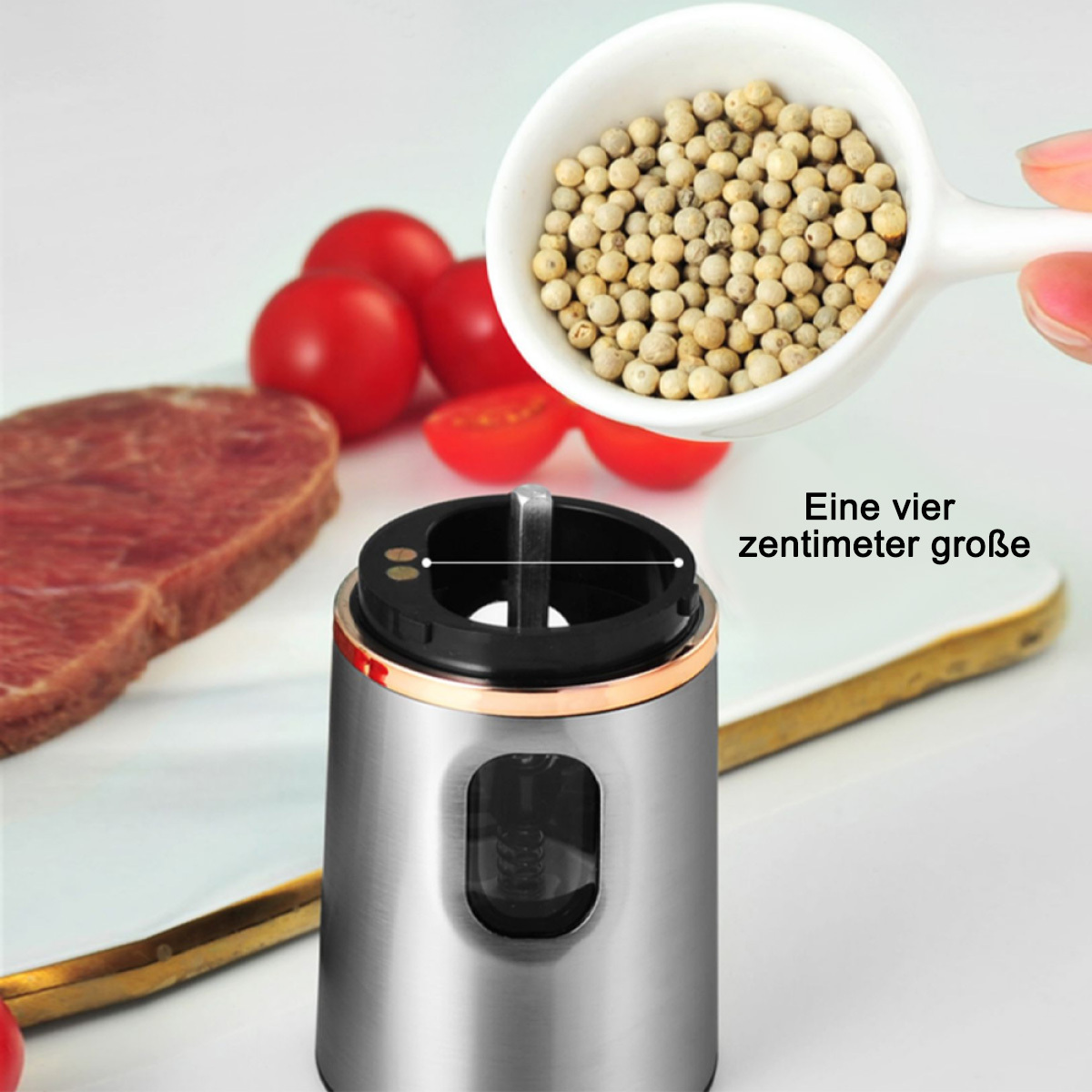 Eine Pfeffermühle, in die Pfefferkörner gegossen werden, neben Steak und Tomaten.