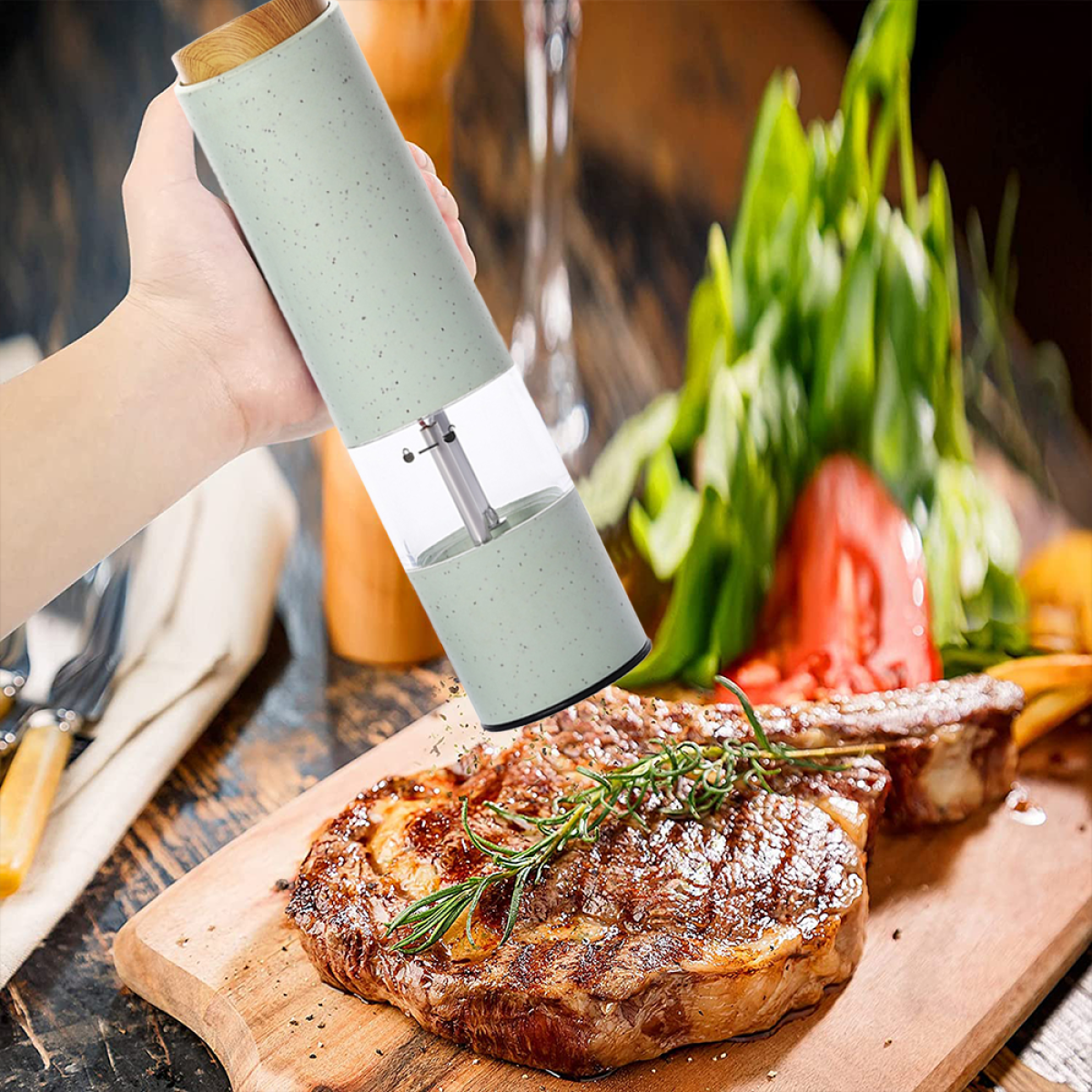Hand benutzt eine Pfeffermühle über einem Steak auf einem Holzbrett mit Rosmarinzweig.