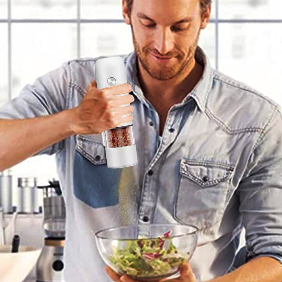 Mann in einer Küche, der einen Pfeffermühle über einer Salatschüssel hält. Lächelt, bereitet Essen zu.