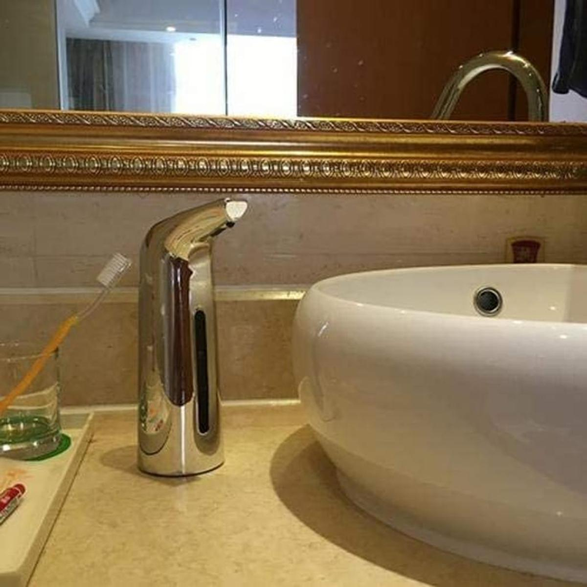 Badezimmer mit silbernem Seifenspender, Waschbecken, Spiegel und Zahnbürste im Glas.