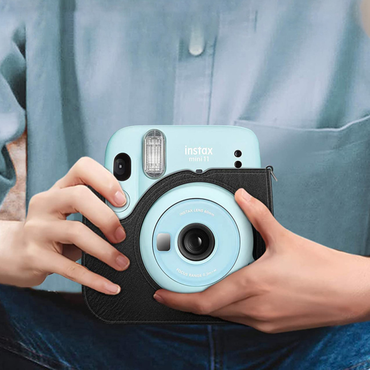 Eine Person hält eine hellblaue Instax Mini 11 Kamera in einer schwarzen Hülle.