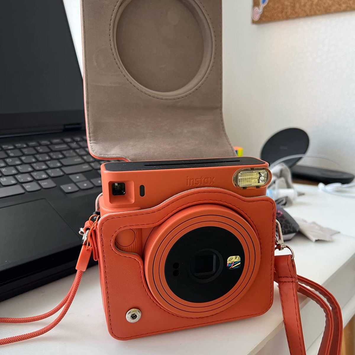Eine orangefarbene Kamera in einem Gehäuse mit Riemen, neben einem Laptop und einer schwarzen Oberfläche.