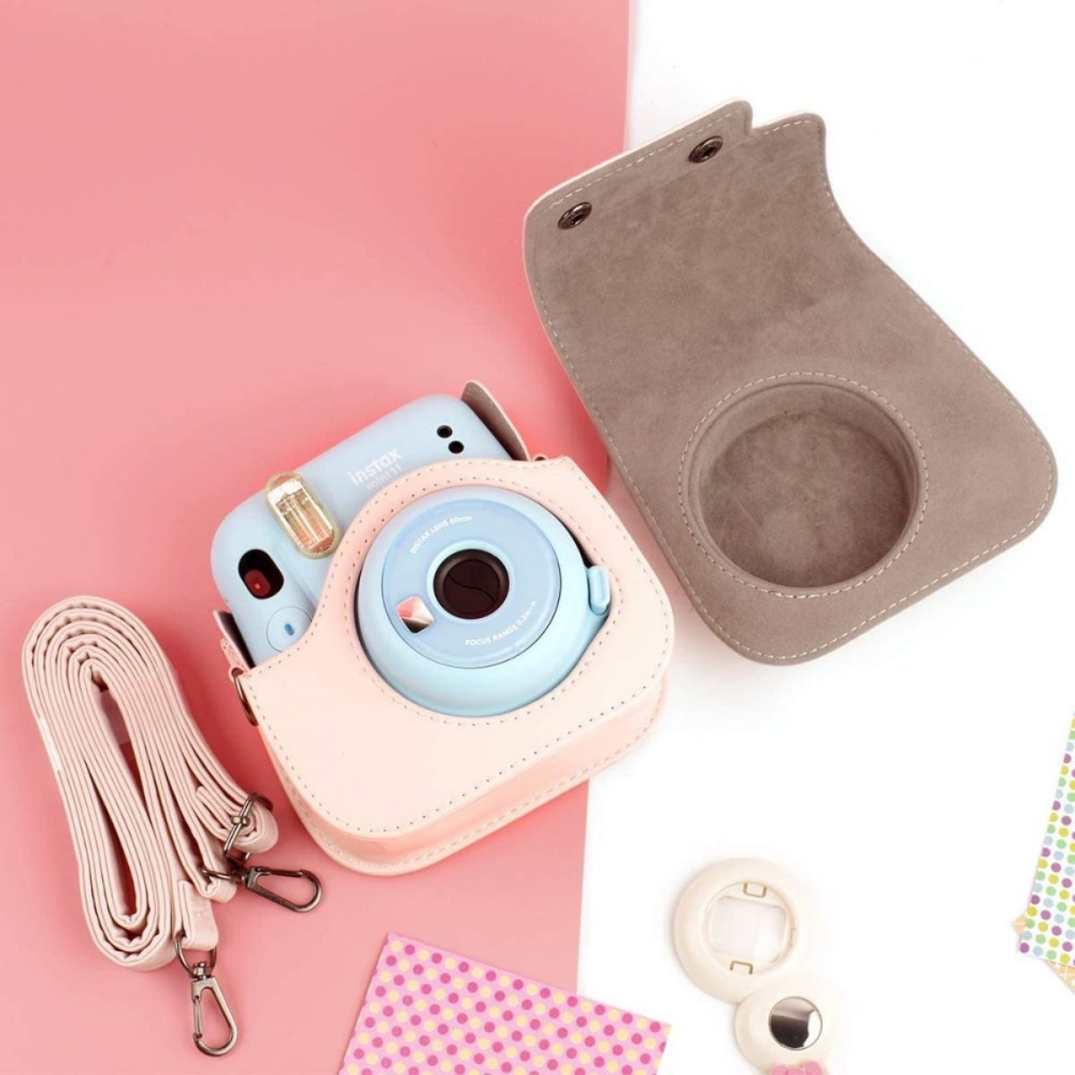 Eine hellblaue Instax-Kamera in einem rosa Etui, Trageriemen und geöffnetes Etui daneben.
