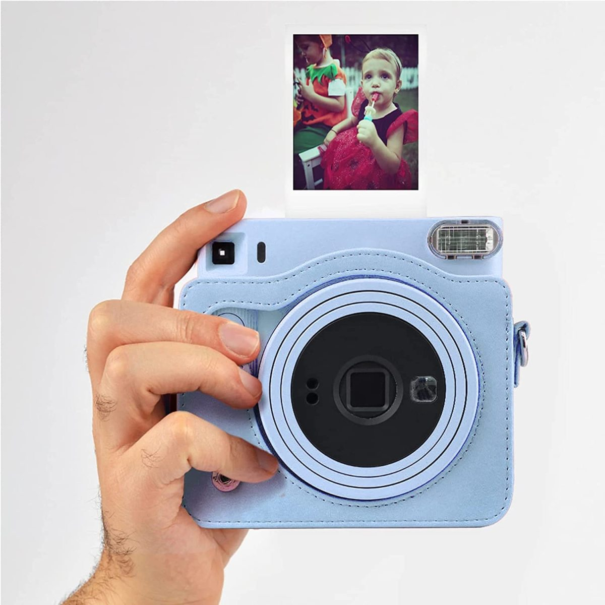 Hand hält hellblaue Sofortbildkamera mit Foto. Kamera hat Objektiv und Blitz.