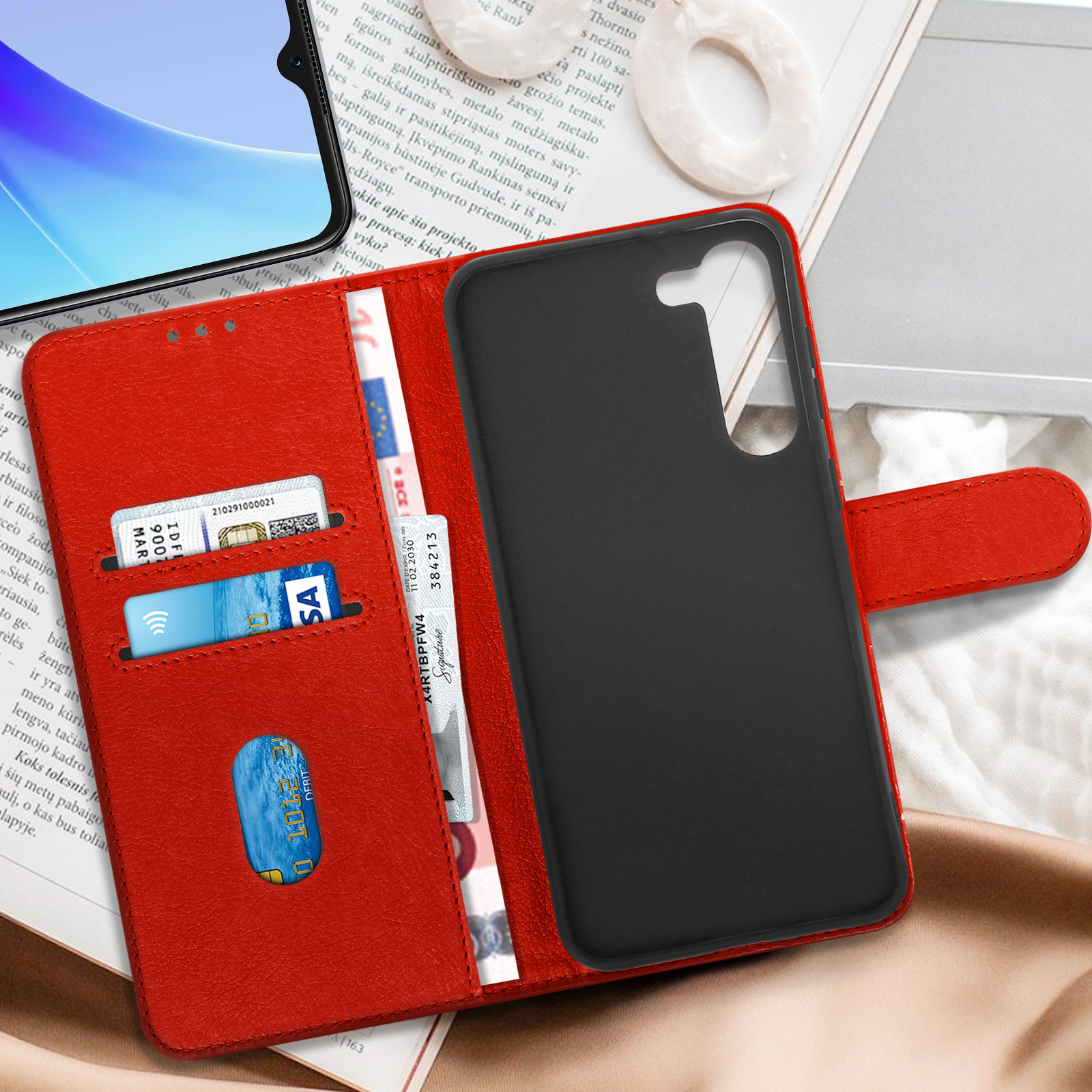 Custodia rossa per telefono con carte e telefono. Lo sfondo è un libro.