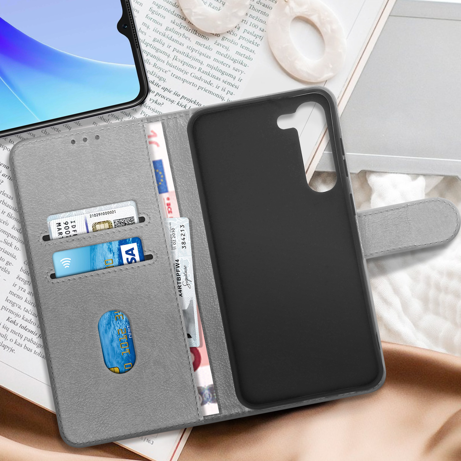 Graues Brieftaschentui mit Karten und Geld. Daneben ist ein Smartphone teilweise sichtbar.