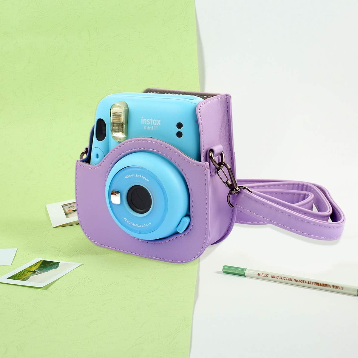Blaue Instax Mini 11 Kamera in einem lila Etui mit Riemen und grünem Marker.