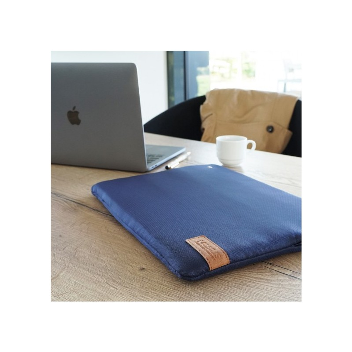 Un portátil en una funda azul sobre una mesa de madera. Hay una taza y un bolígrafo sobre la mesa. El fondo está desenfocado.