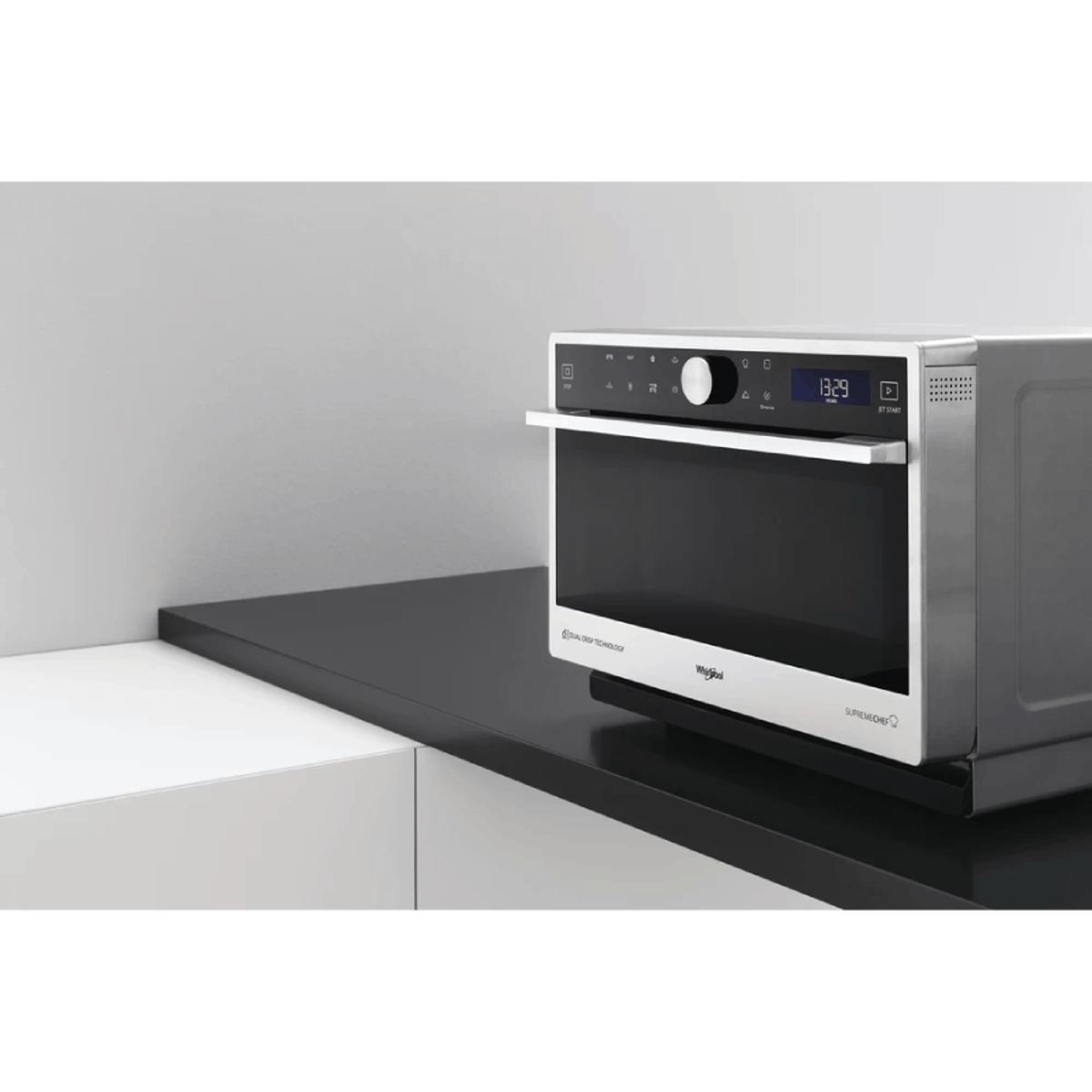 Srebrna kuchenka mikrofalowa na czarnej powierzchni z białą ścianą w tle. Wyświetlacz pokazuje czas.