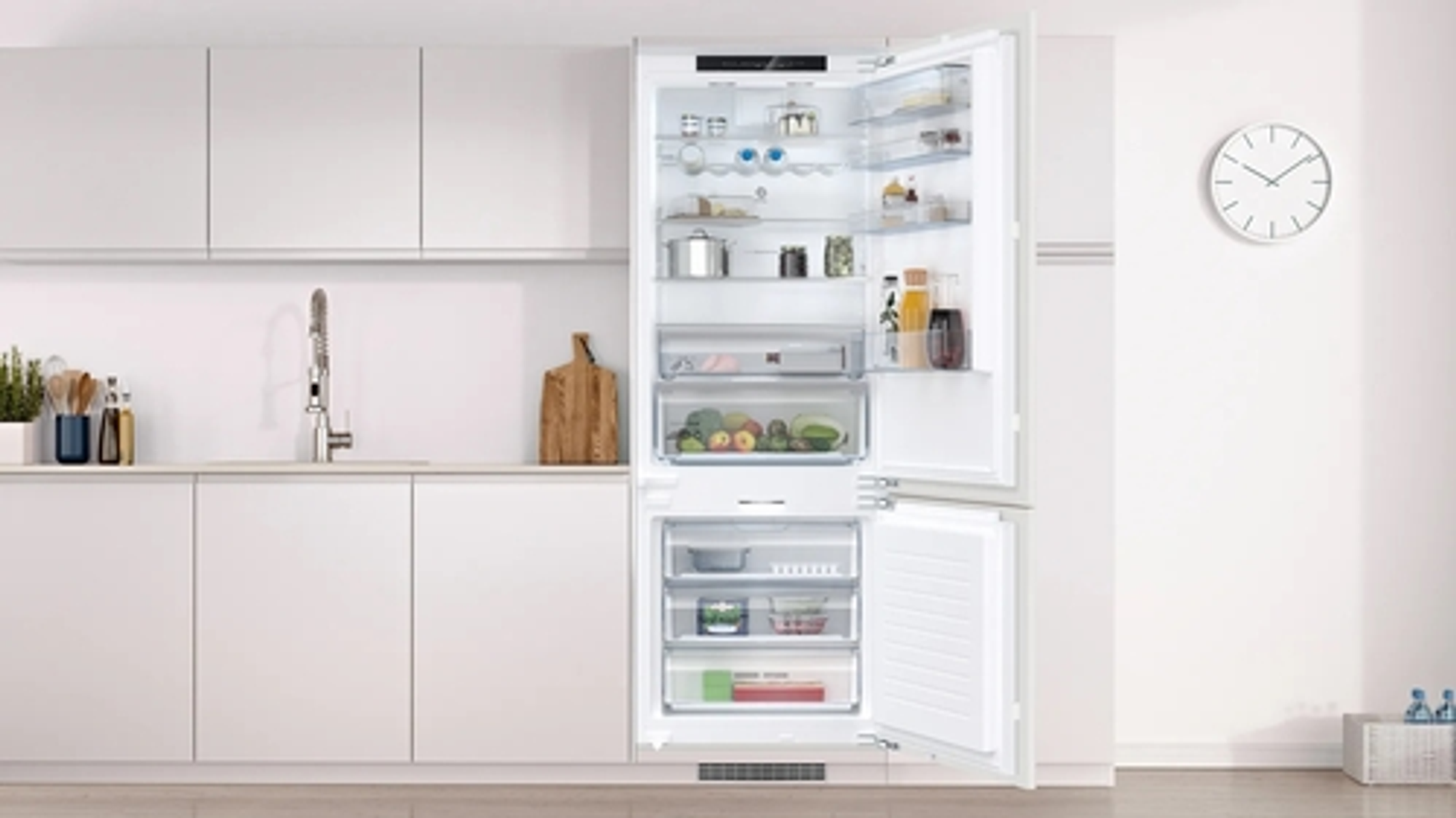 Refrigerador abierto con alimentos dentro, ambiente de cocina blanca.
