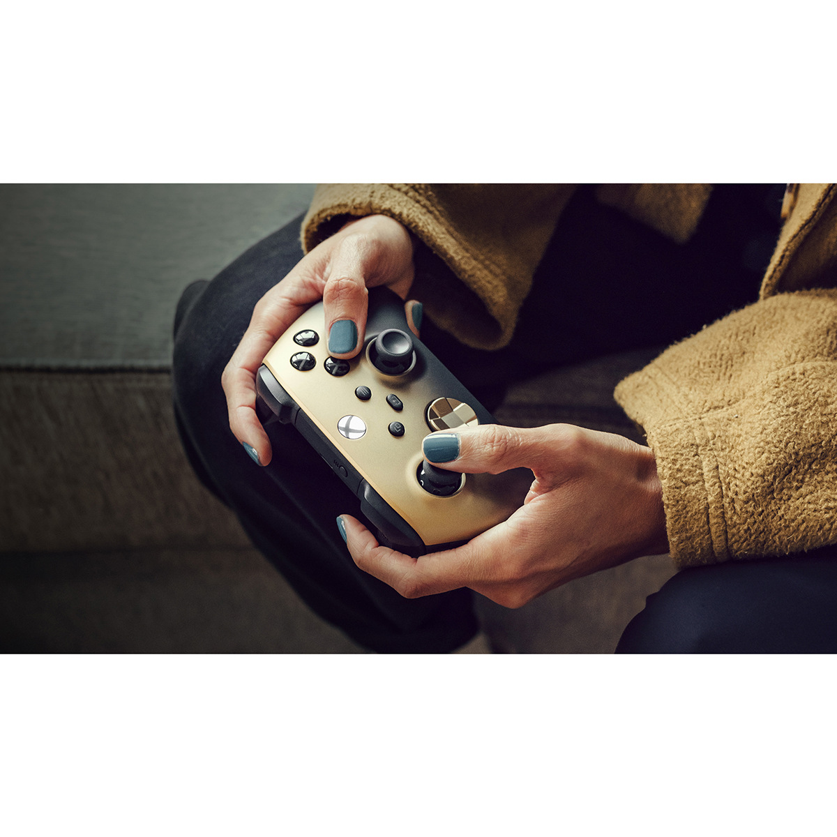 Person hält einen gold-schwarzen Xbox-Controller. Die Person hat blauen Nagellack.