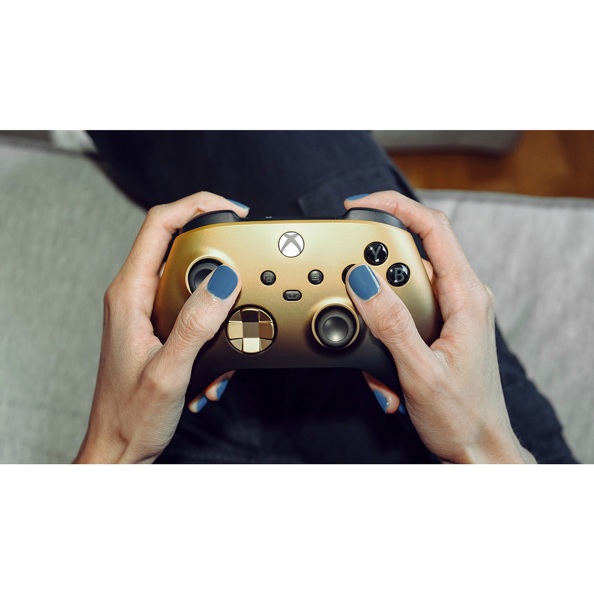 Hände einer Person, die einen gold-schwarzen Xbox-Controller halten. Blauer Nagellack sichtbar.
