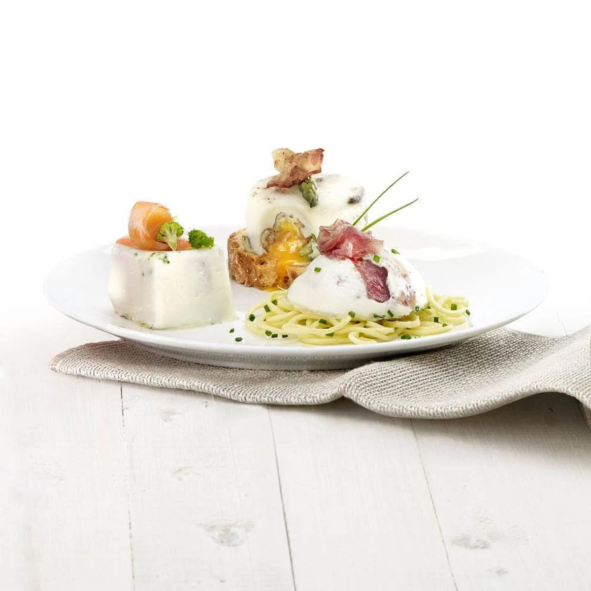 Piatto con tre porzioni gourmet: pasta e altri due piatti, su un tavolo bianco.