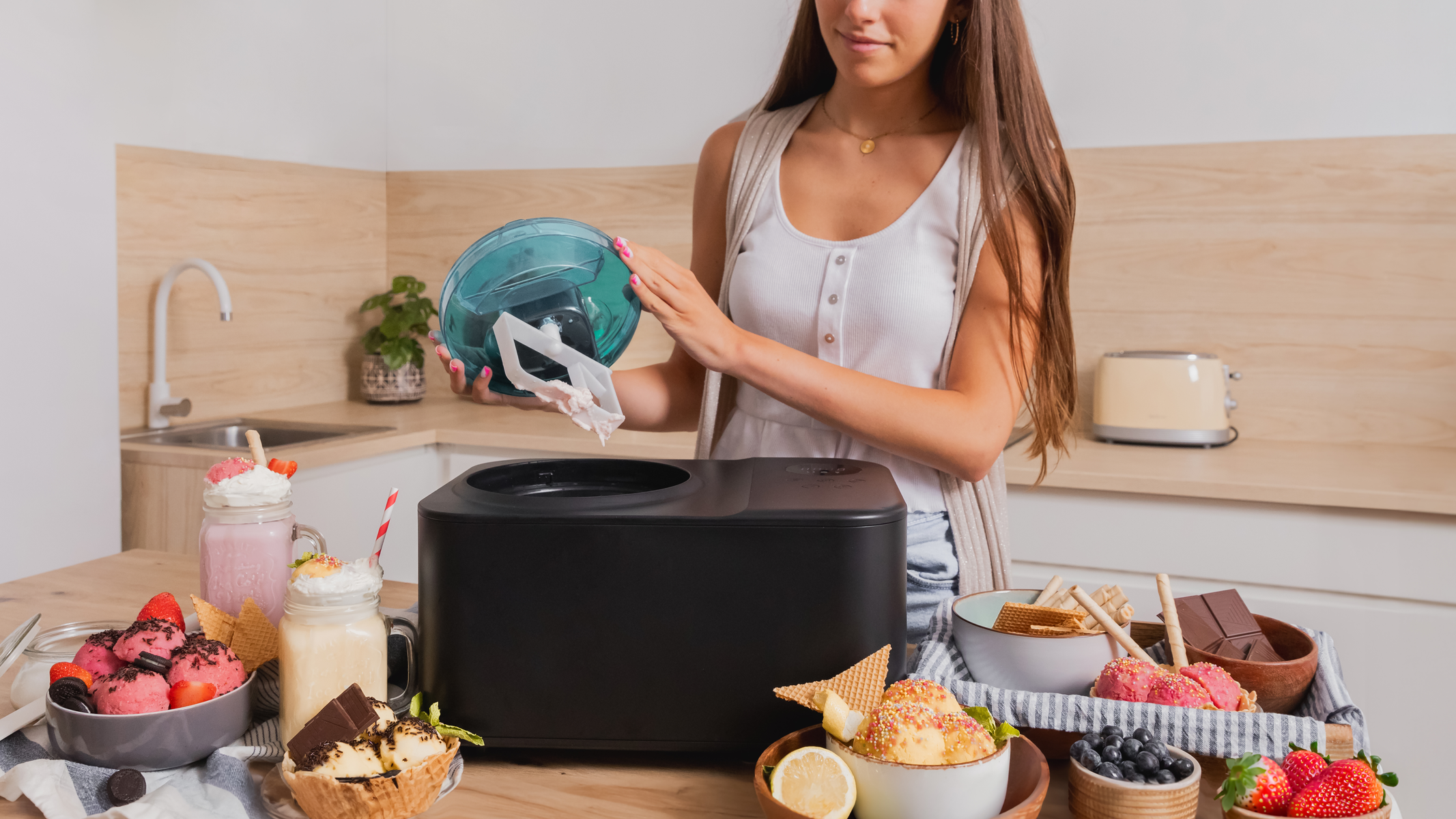 Kobieta robiąca lody, otoczona składnikami i gotowymi deserami na wyspie kuchennej.