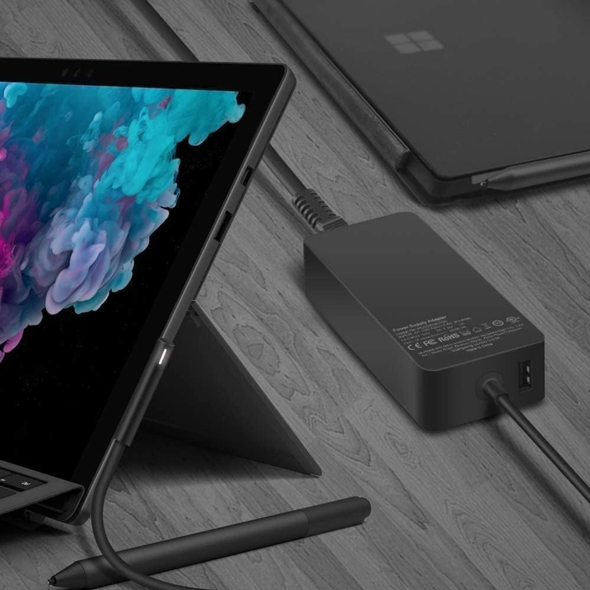 Portátil, cargador y Surface Pen sobre una superficie de madera.