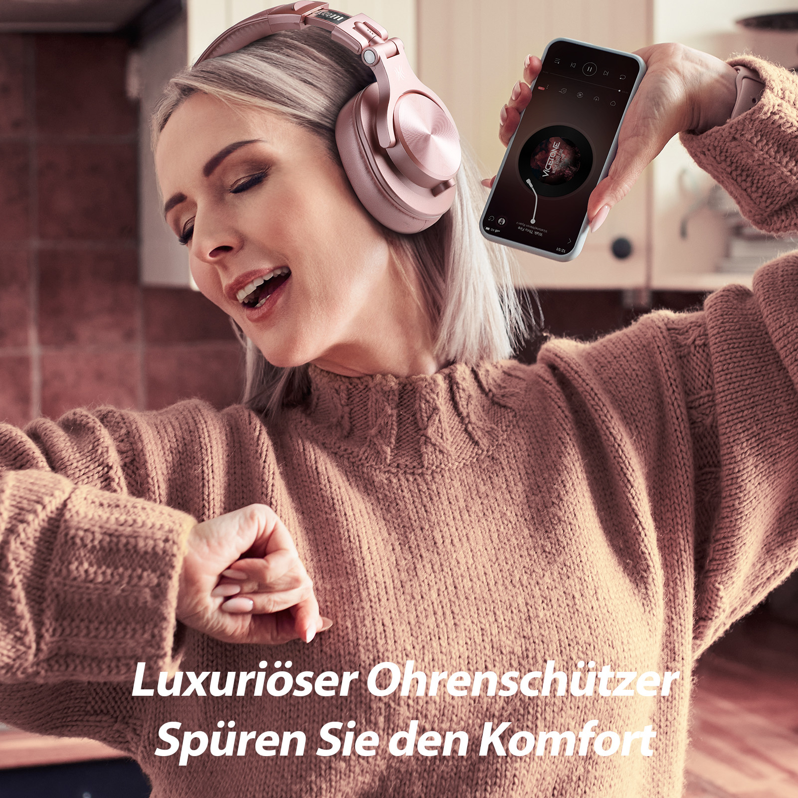 Frau mit rosa Kopfhörern hält ein Handy mit Musik. Der Hintergrund ist eine Küche.