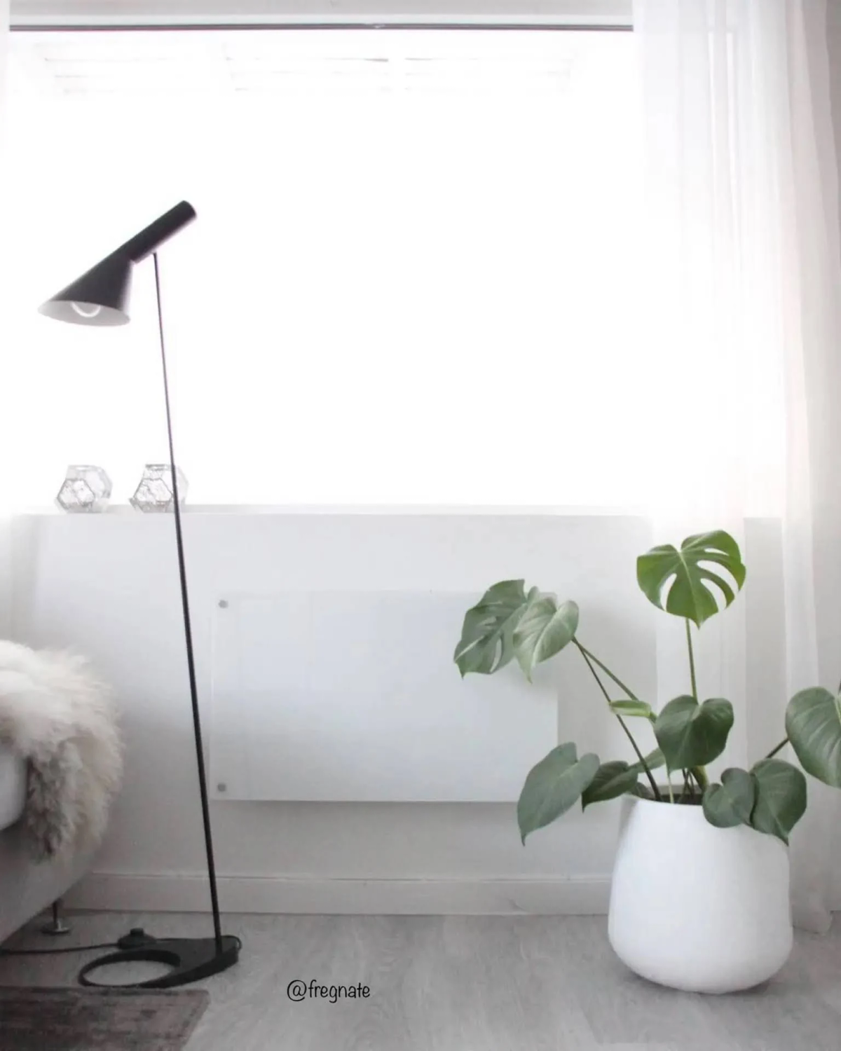 Interior con lámpara de pie negra, pared blanca, planta y ventana con cortinas.
