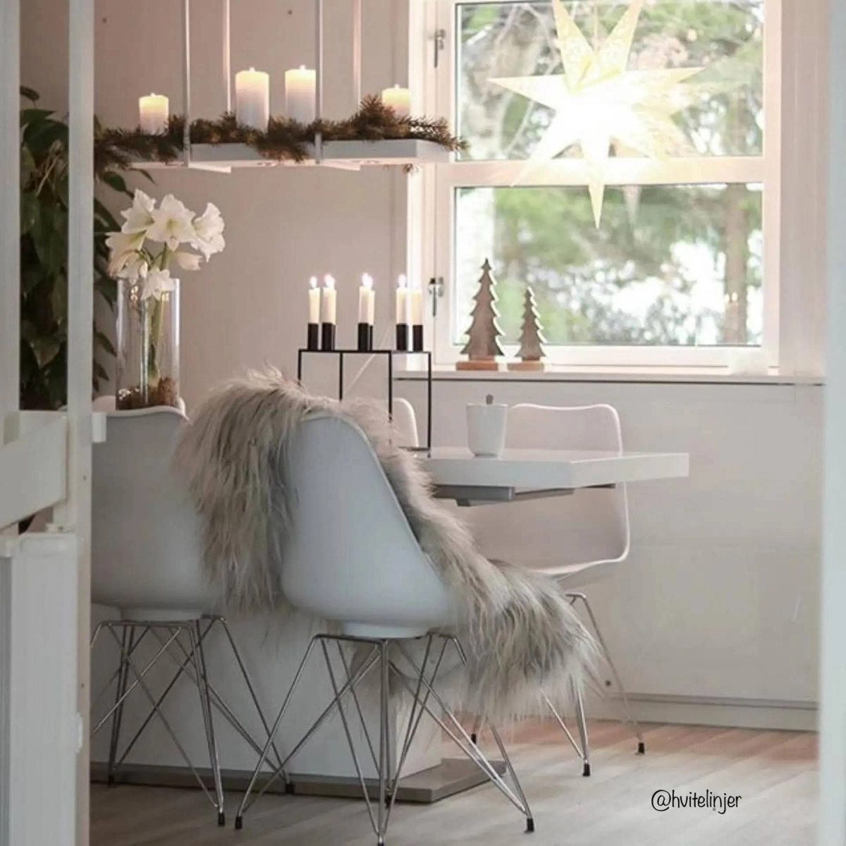 Un comedor con velas y una ventana. Hay sillas blancas y una manta de piel en una.
