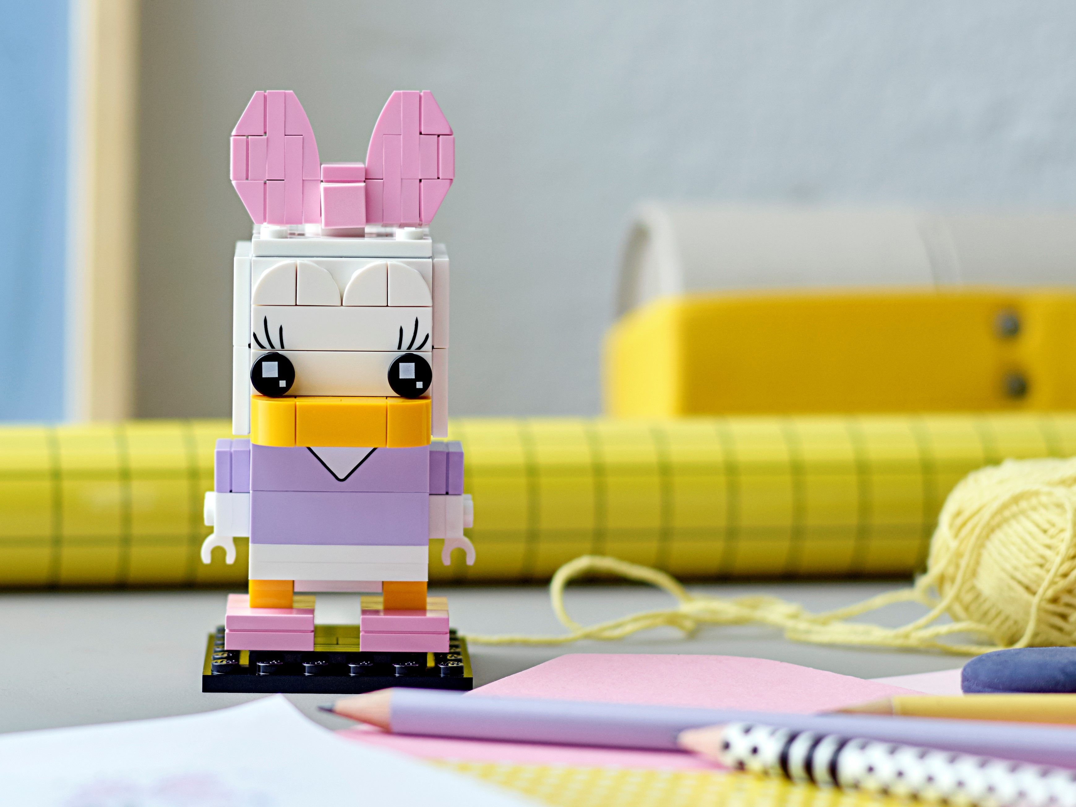 Eine Lego Daisy Duck Figur steht auf einem Tisch mit Stiften und Papier.