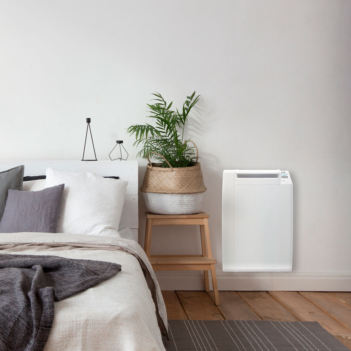 Dormitorio con cama blanca, planta y calefactor. Suelo de madera y alfombra.