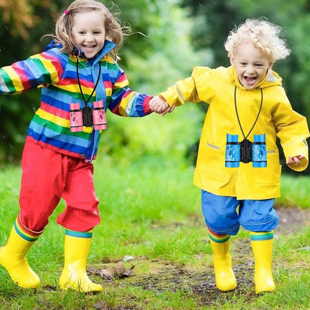 Zwei Kinder tragen Regenkleidung und halten Ferngläser. Sie sind draußen, lächeln, im Regen.