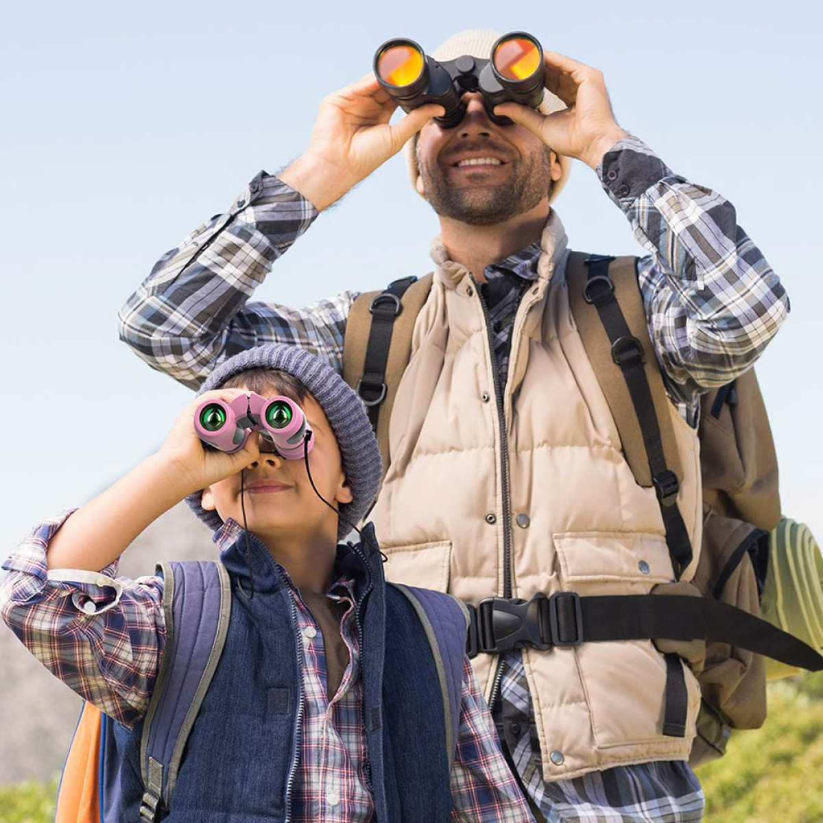 Ein Vater und ein Sohn schauen durch ein Fernglas. Der Sohn trägt ein rosa Paar.