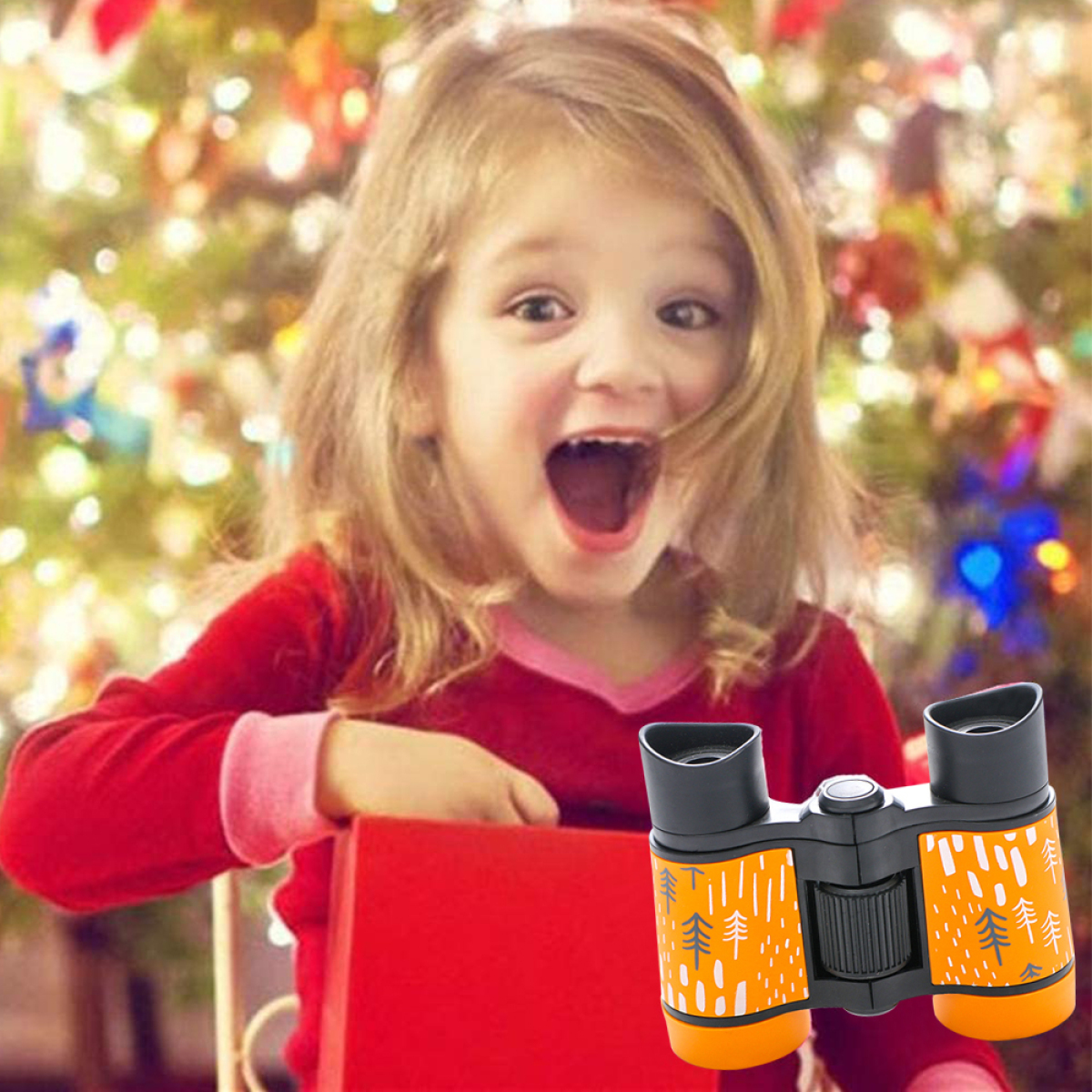 Ein Mädchen mit offenem Mund, das eine rote Geschenkbox hält. Fernglas im Vordergrund. Weihnachtsbaum im Hintergrund.
