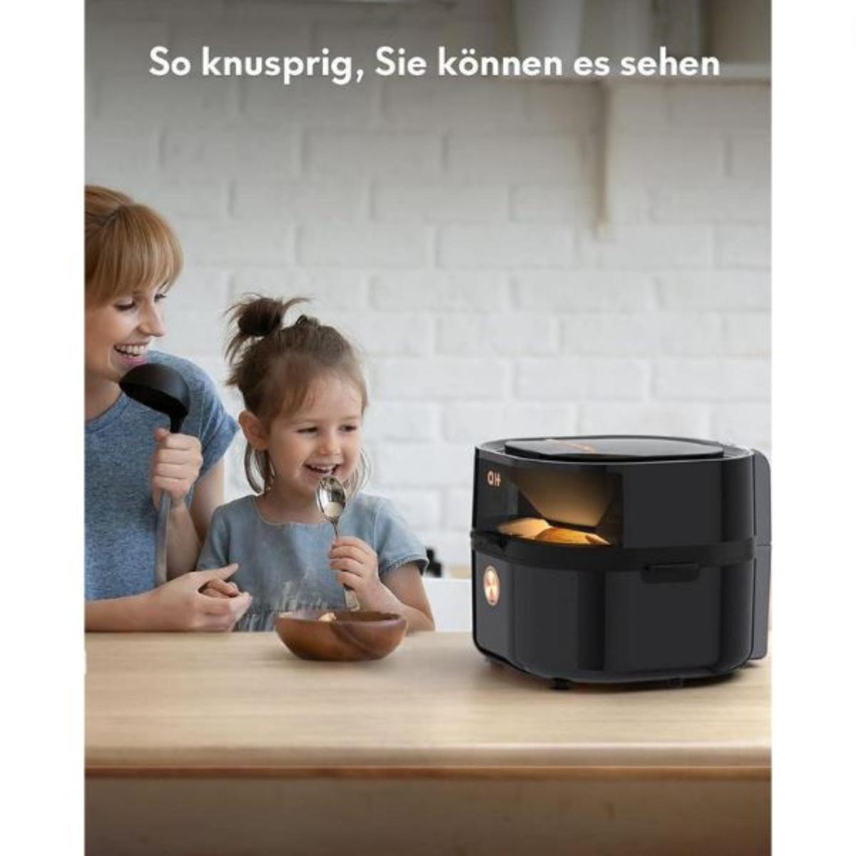 Eine Frau und ein Mädchen lächeln und halten eine Kelle und einen Löffel in der Nähe einer schwarzen Fritteuse.