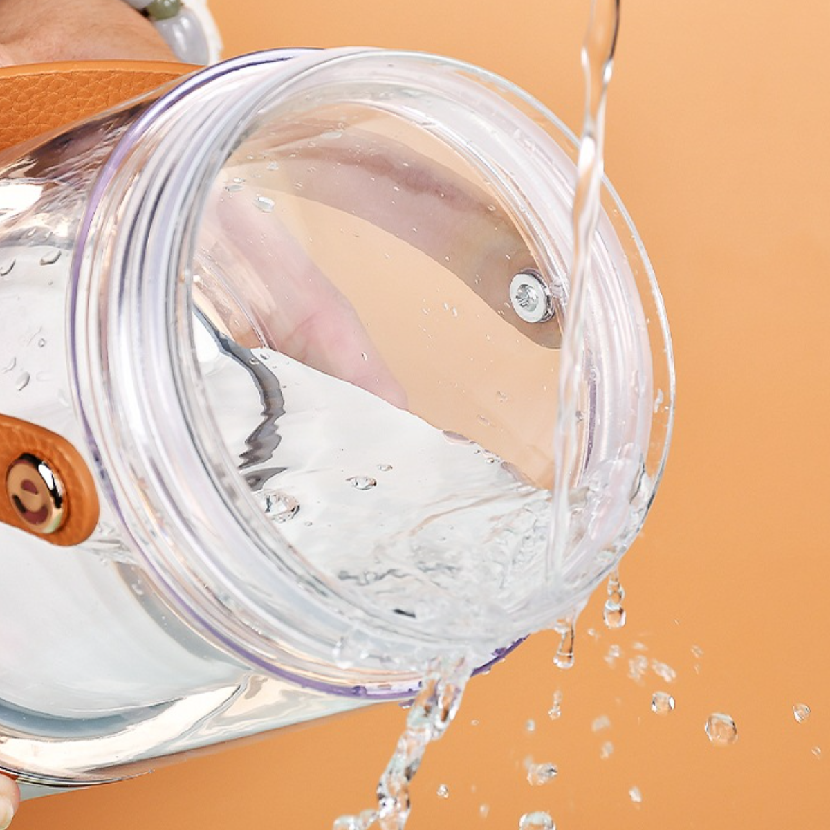 Klares Wasser, das in ein klares Glas mit braunem Griff auf orangefarbenem Hintergrund gegossen wird.