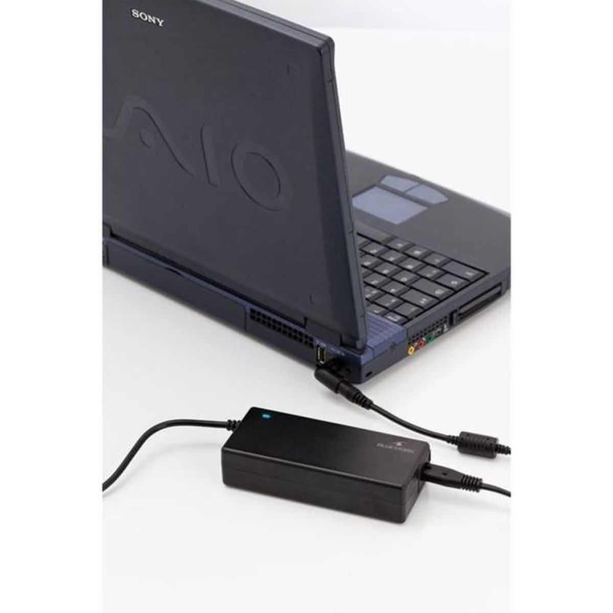Schwarzer Laptop, der an ein schwarzes Netzteil auf einer weißen Oberfläche angeschlossen ist.