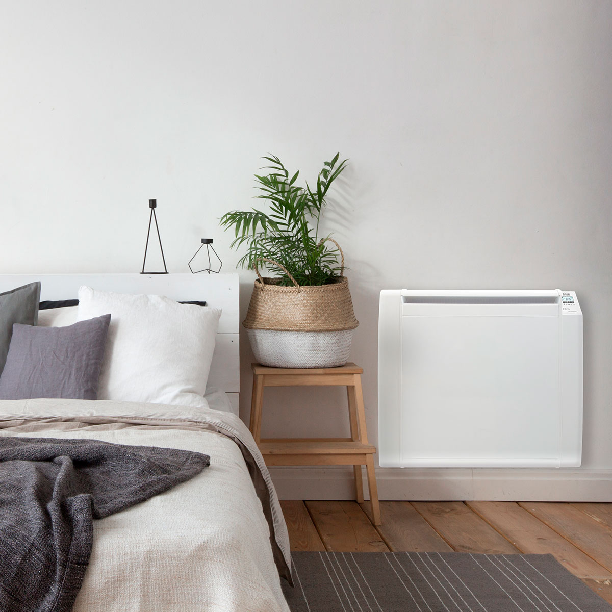Dormitorio con cama, calefactor y planta en un taburete. Las paredes son blancas.