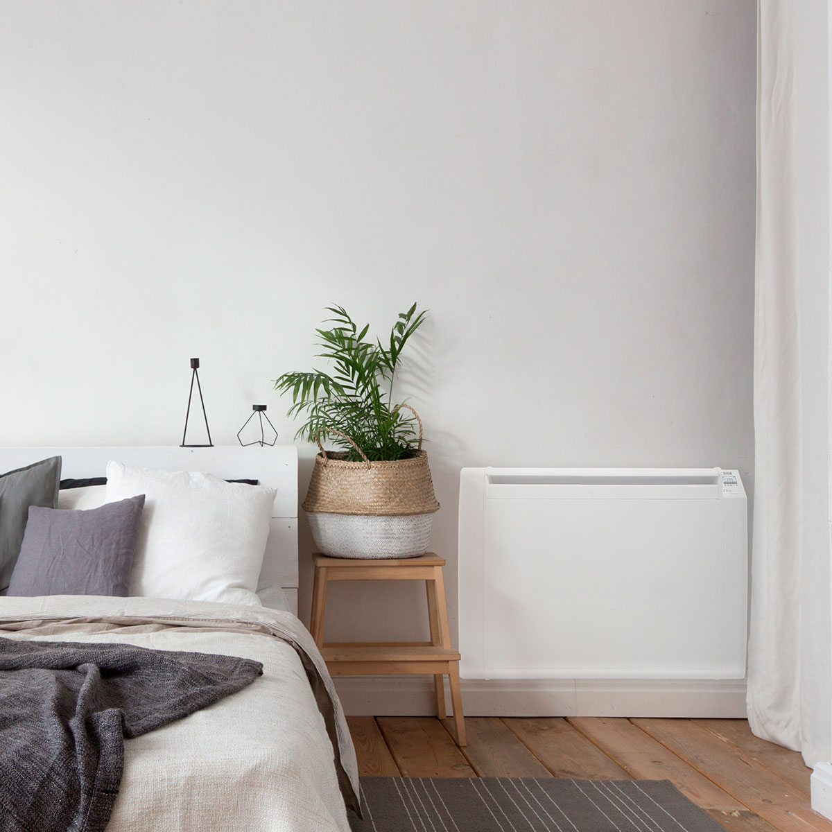 Escena de dormitorio con cama, planta en taburete y calefactor blanco.