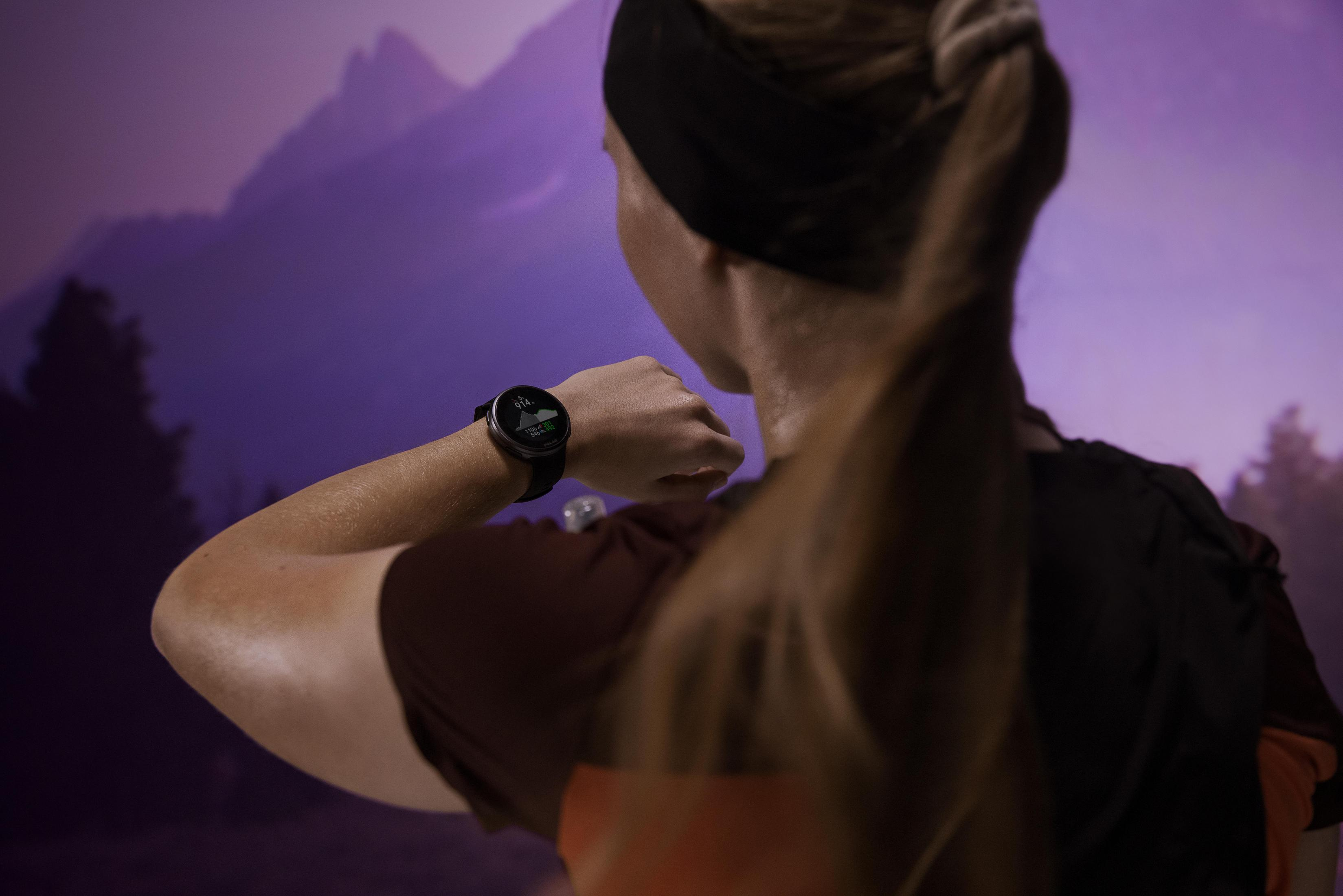 Persona che guarda uno smartwatch, braccio teso, di fronte a uno sfondo viola.