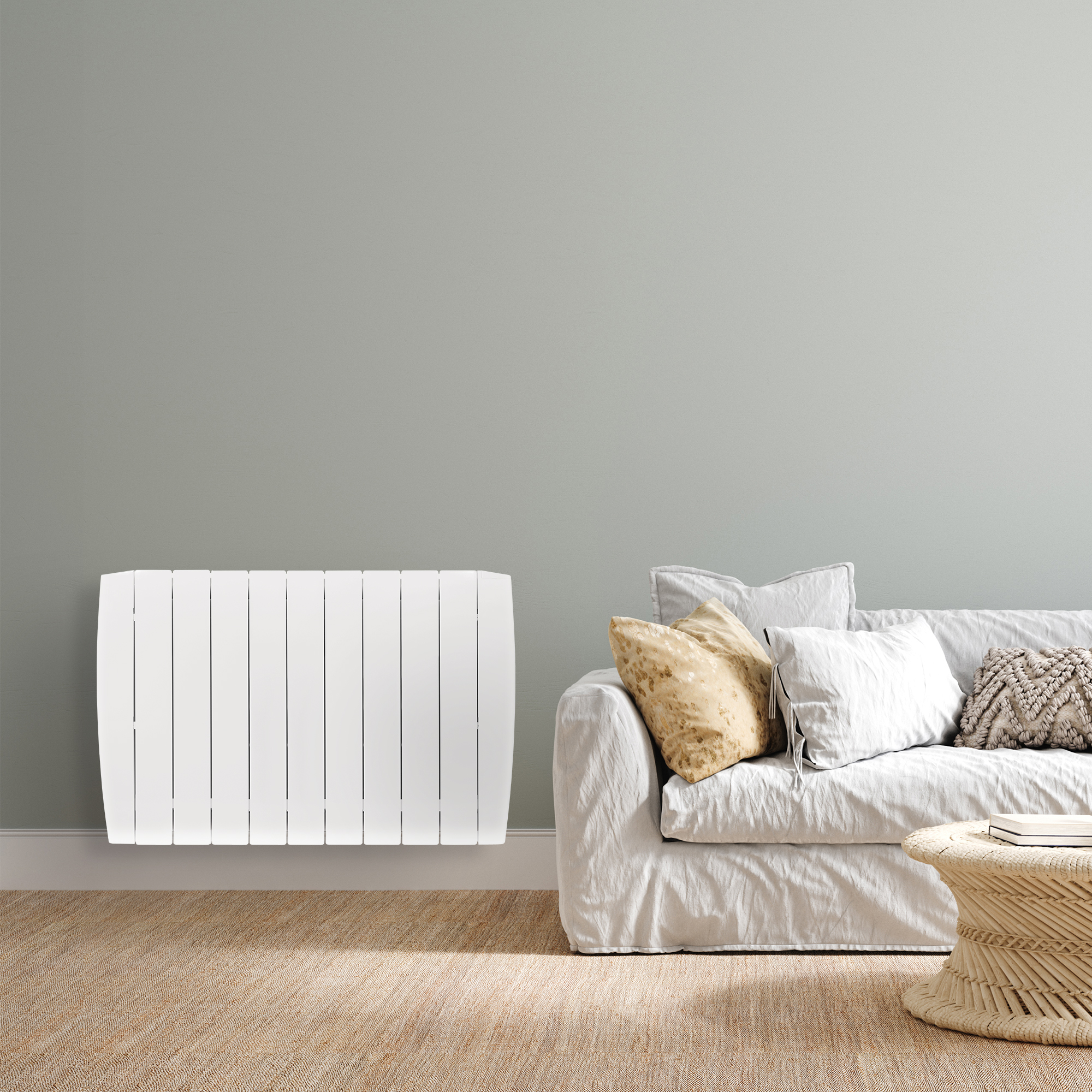 Radiador eléctrico blanco junto a un sofá blanco con almohadas y una mesa pequeña.