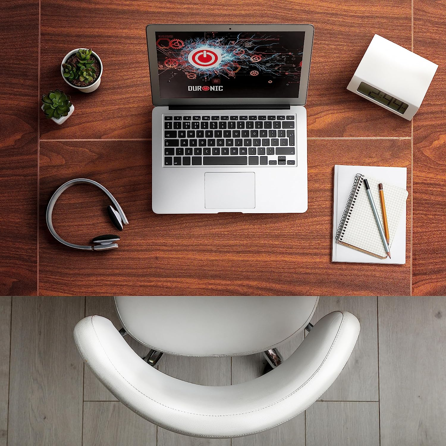 Ein Laptop auf einem Holztisch. Ein Notizblock, Kopfhörer, ein Stift und ein weißer Stuhl sind ebenfalls zu sehen.