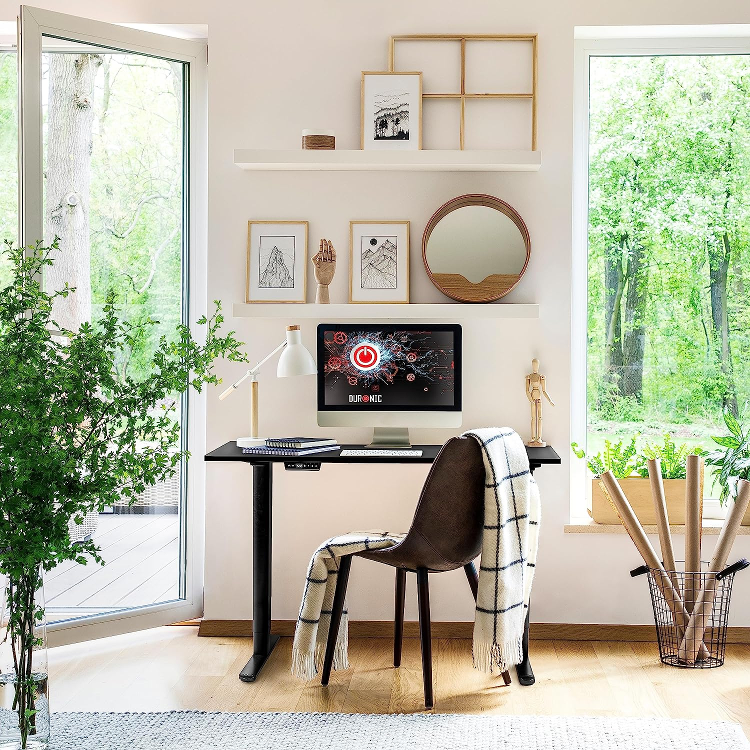 Schreibtisch mit Computer, Stuhl und Fenster mit Bäumen. Regale mit Fotos und Dekoration. Grüne Pflanzen.