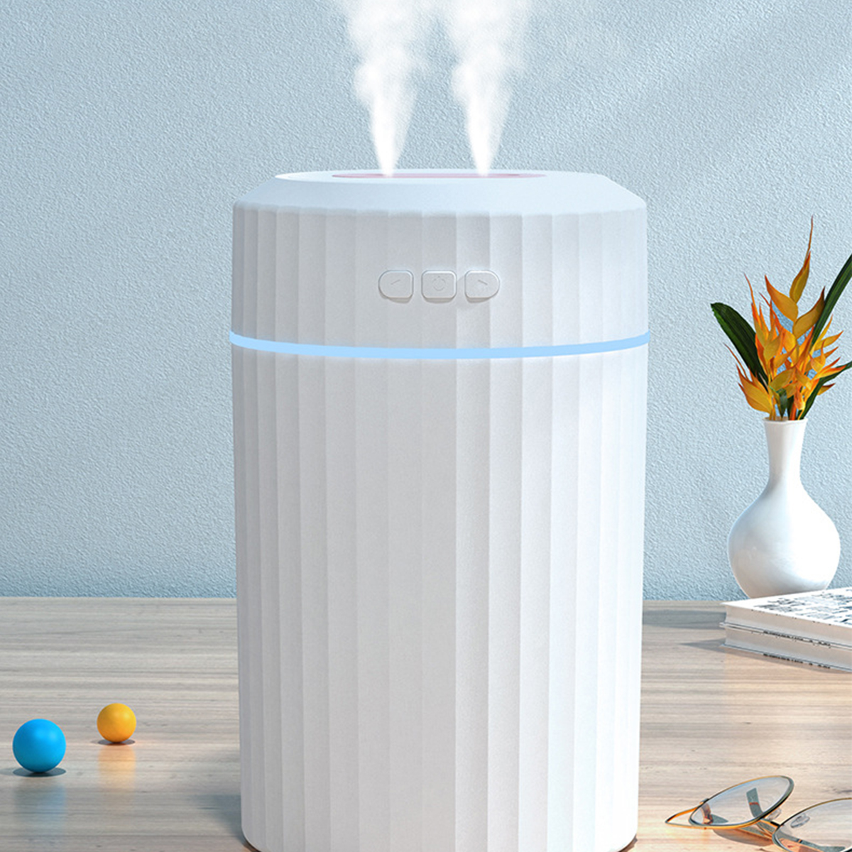 Weißer Luftbefeuchter, Dampf steigt auf, blaues Licht, Vase mit Blumen und zwei kleine bunte Bälle.