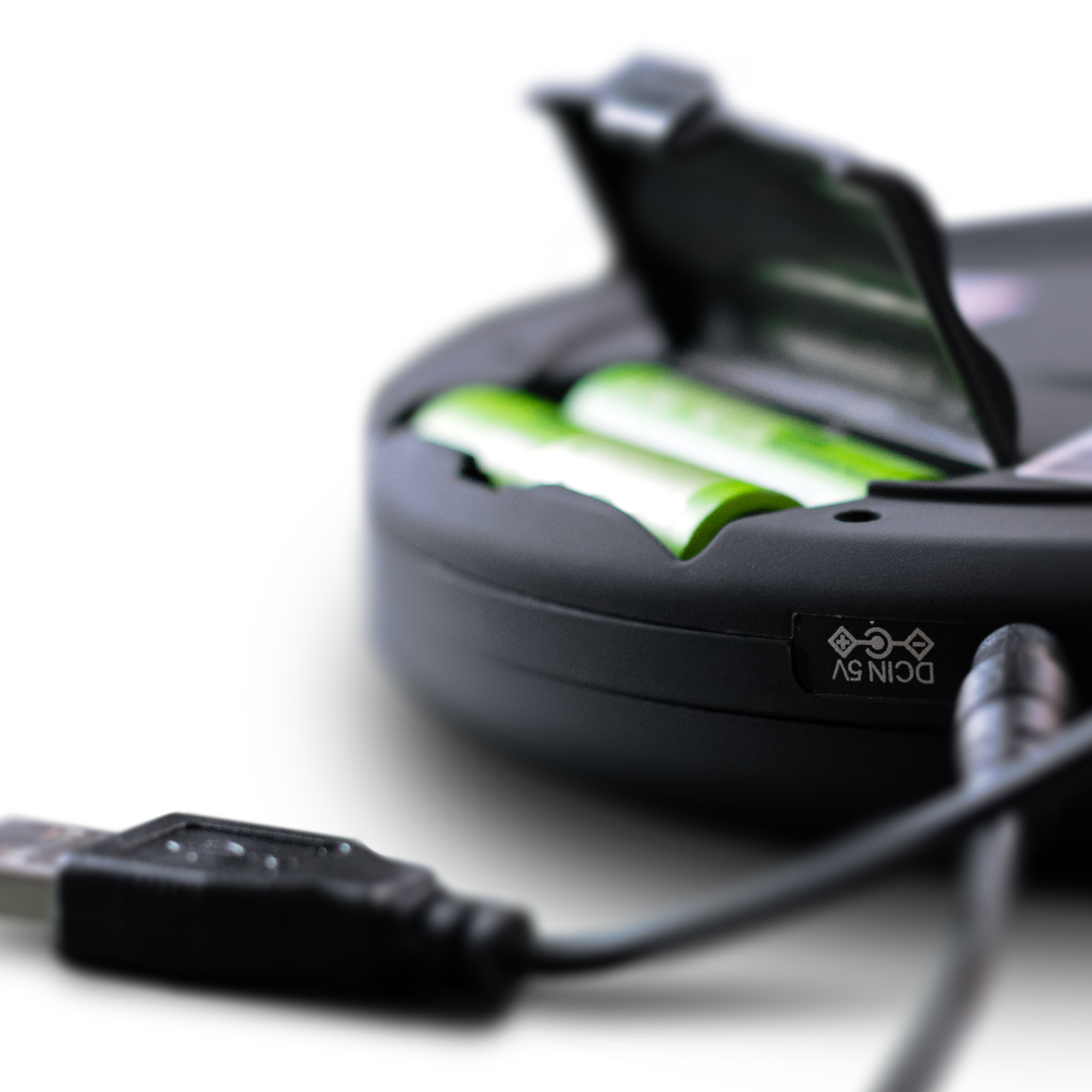 Schwarzes Gerät mit offenem Fach, das zwei grüne Batterien enthält. Ein USB-Kabel ist angeschlossen.