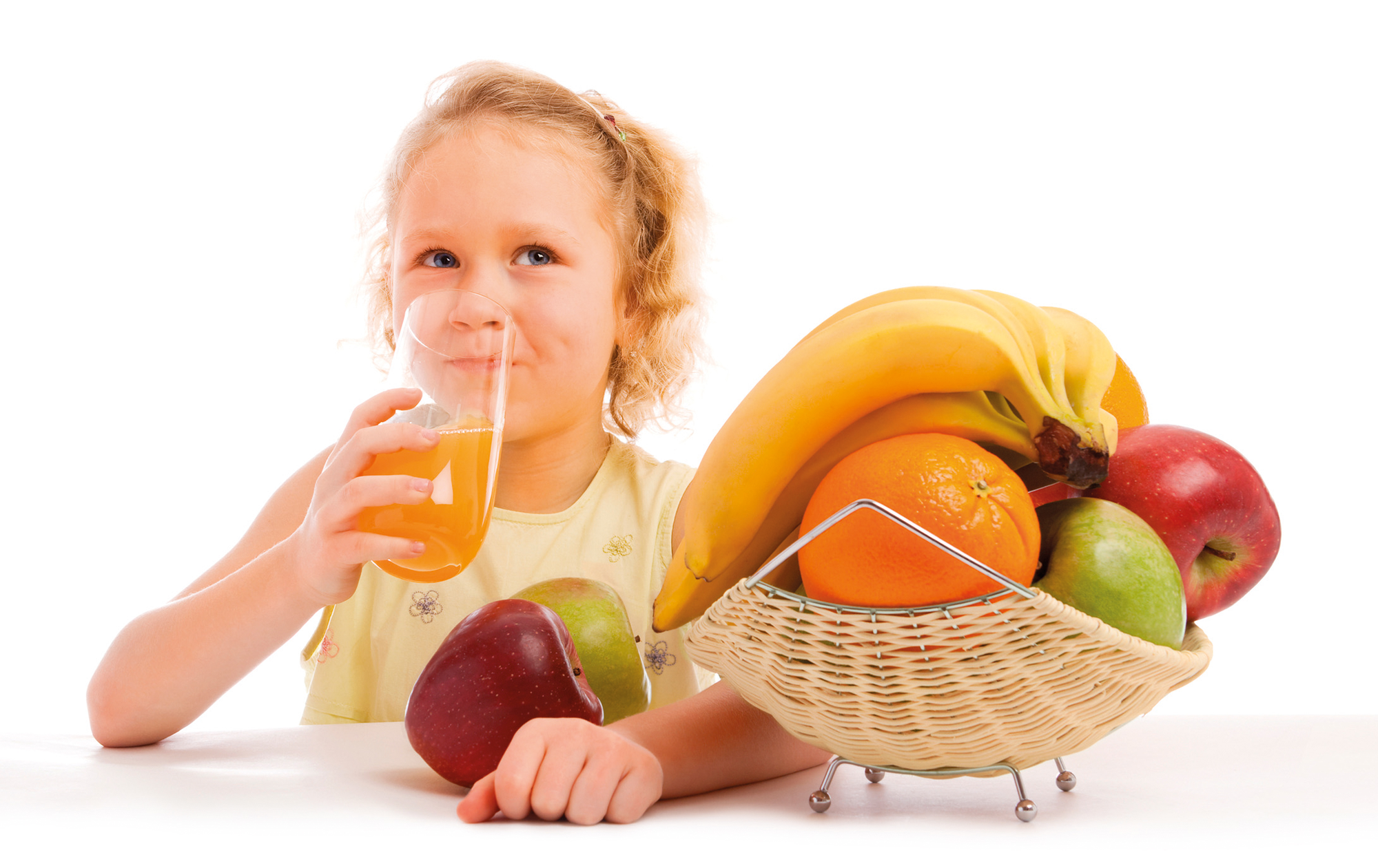 Een meisje drinkt sap uit een glas naast een fruitmand.