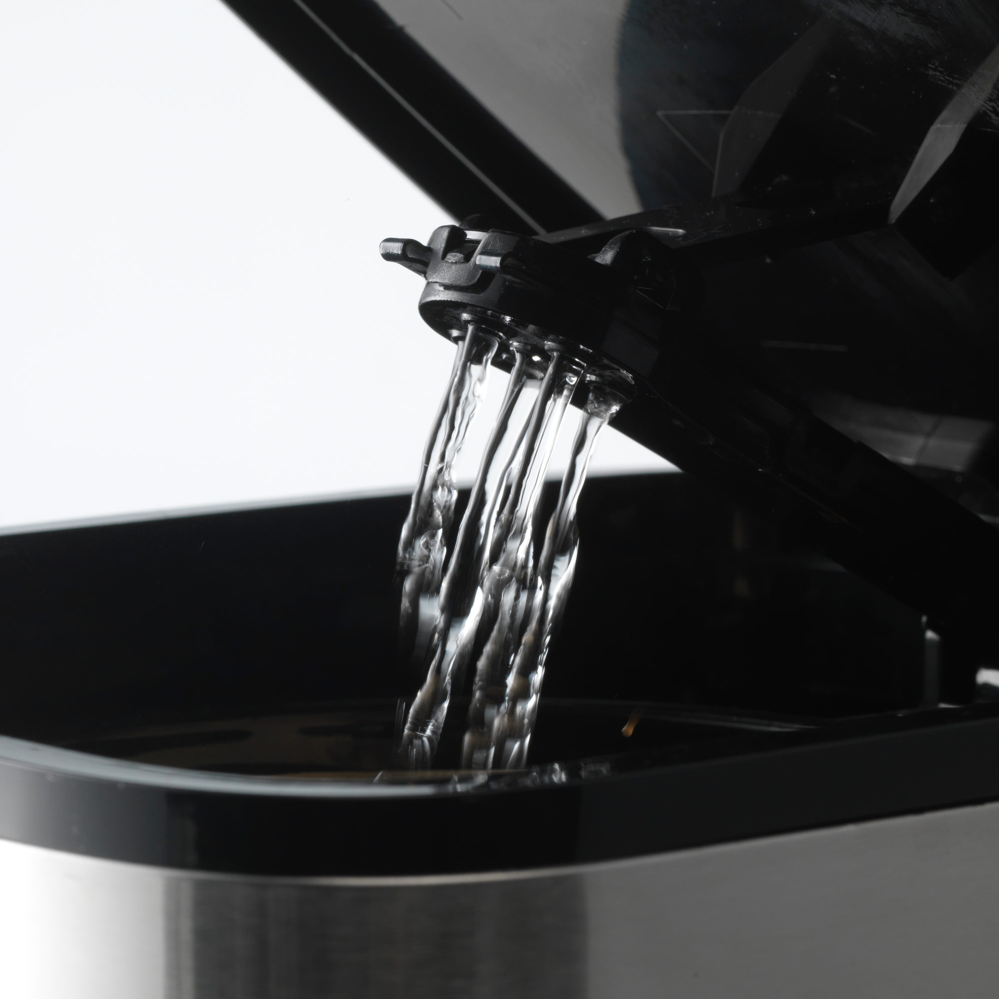 Wasser fließt aus dem Ausguss eines schwarzen Kaffeeautomaten in einen schwarzen Behälter.