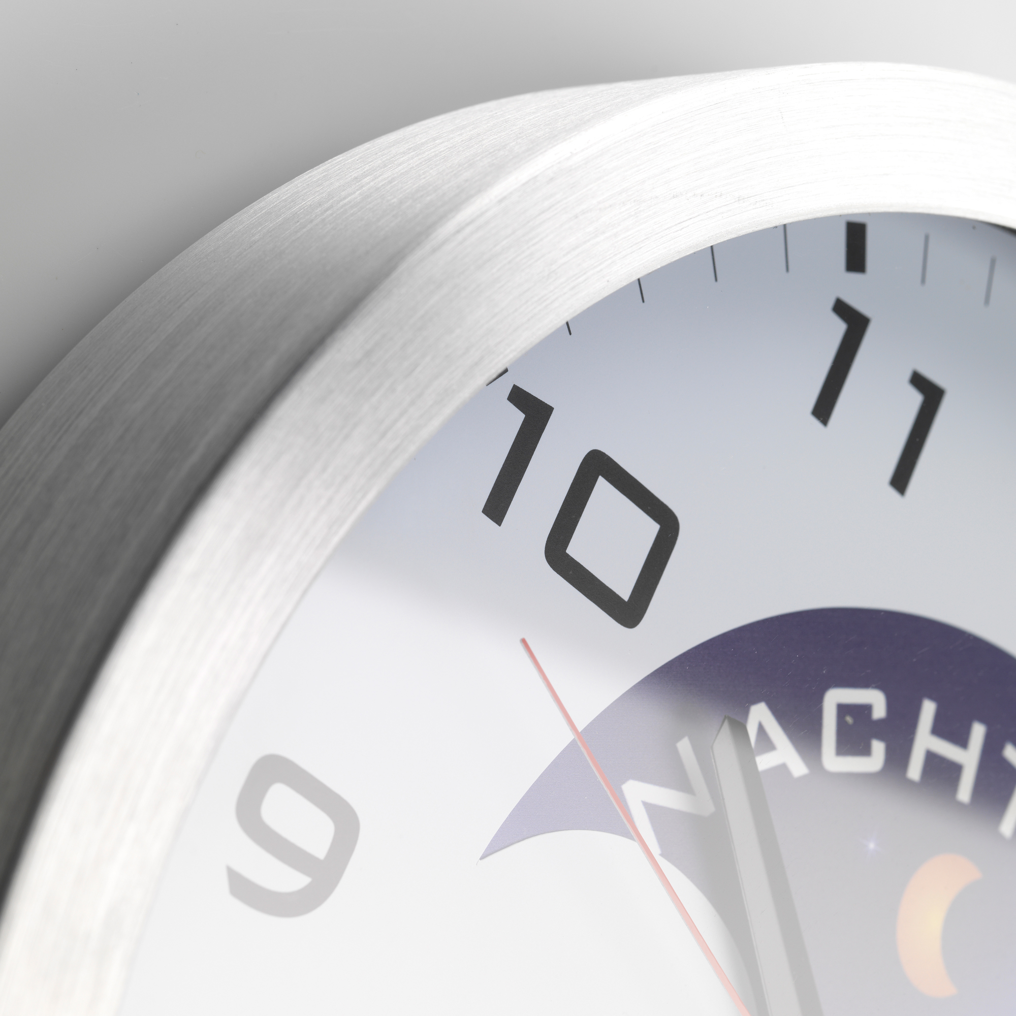 Nahaufnahme einer weißen Uhr mit schwarzen Zahlen bei 9, 10 und 11. Der Hintergrund ist grau.