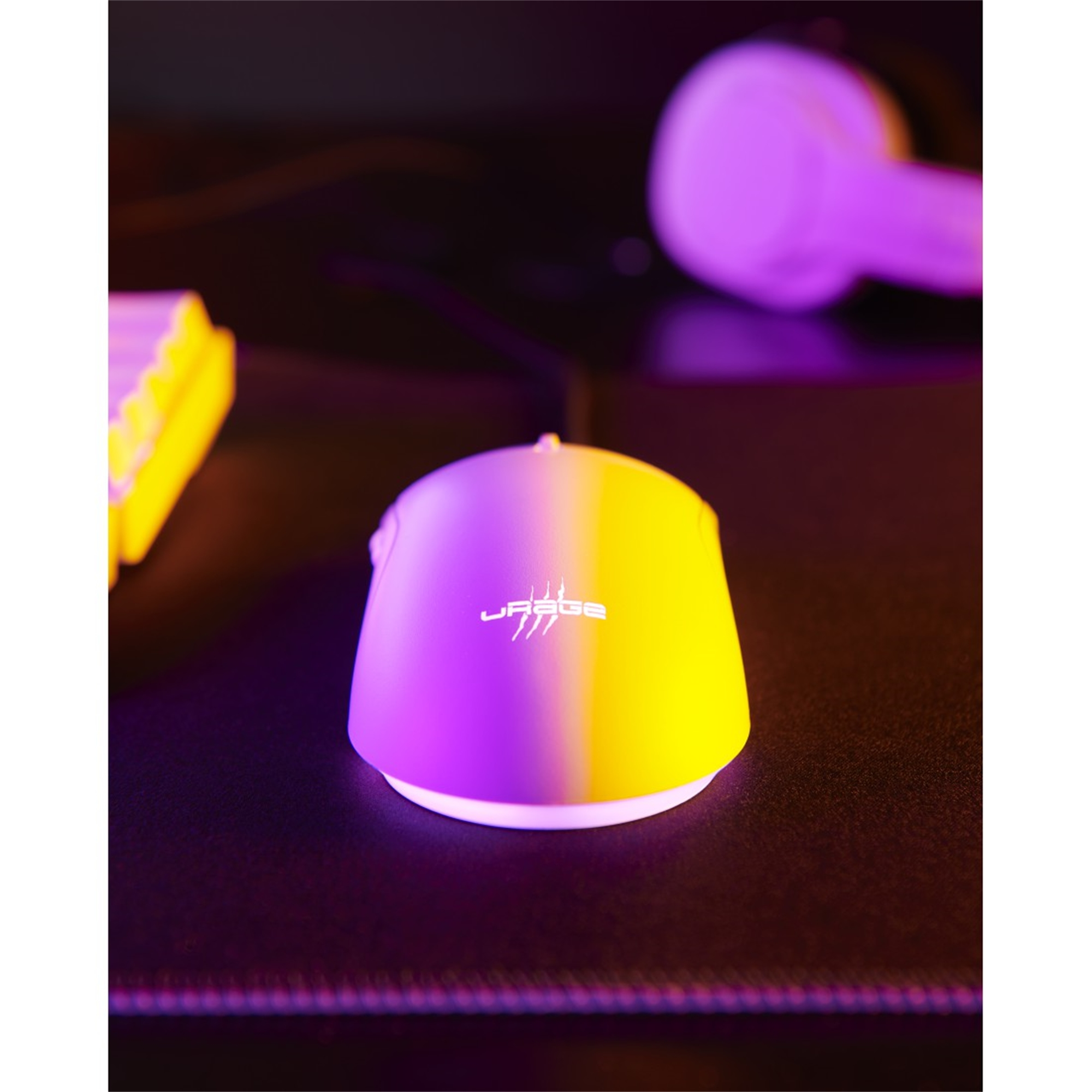 Eine Gaming-Maus mit lila und gelbem Farbverlauf, Logo oben. Tastatur und Kopfhörer im Hintergrund.
