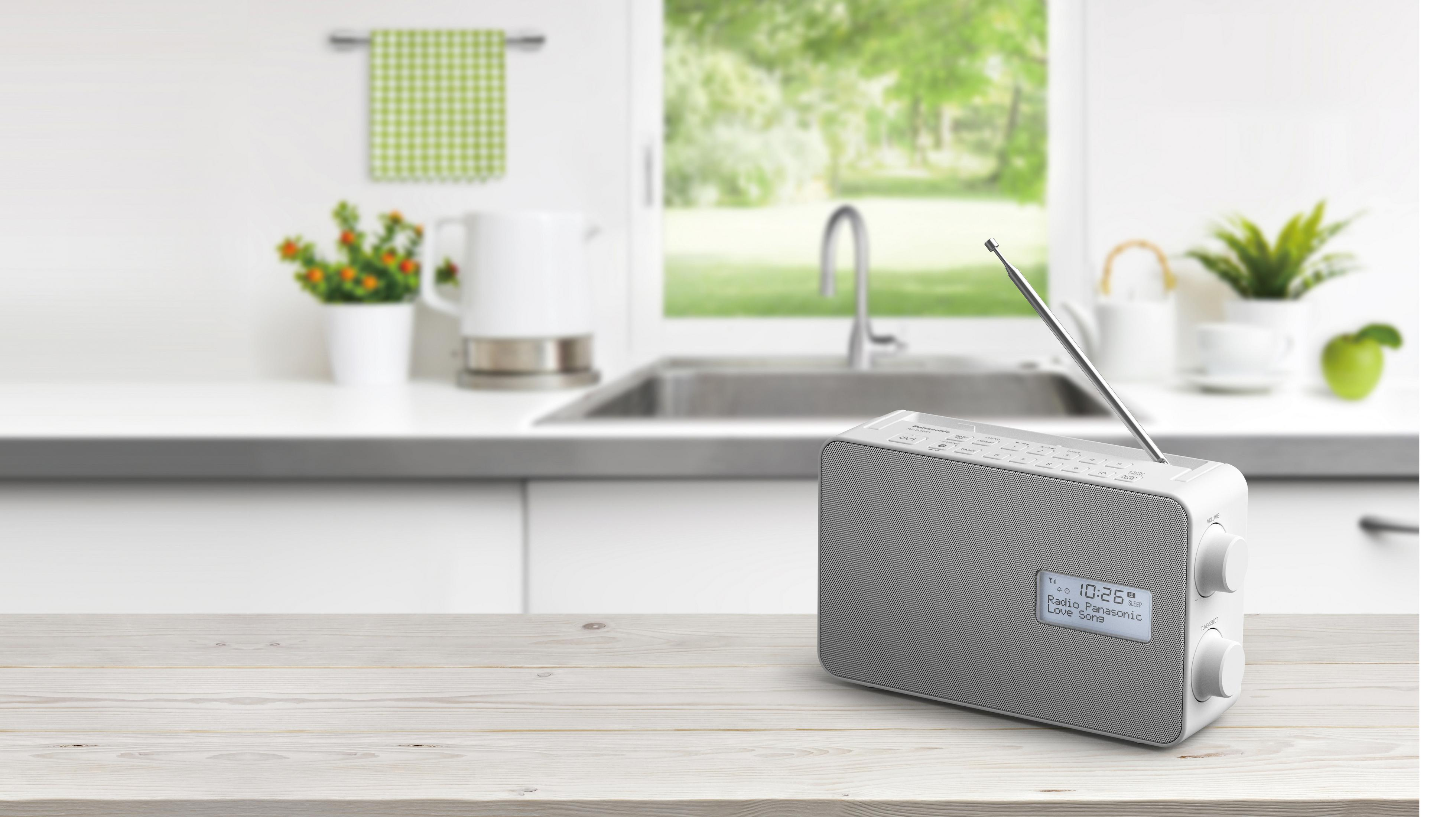 Radio na drewnianym stole w kuchni. Kuchnia ma białe szafki i zielone okno.